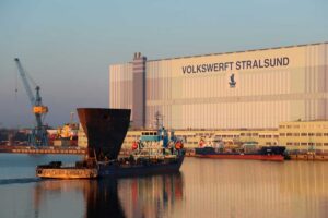 Transportschiff „Aura“ mit dem Vorschiff der „Walther Herwig“ vor der Montagehalle 290 in Stralsund; hinten rechts der Tanker „Annika“