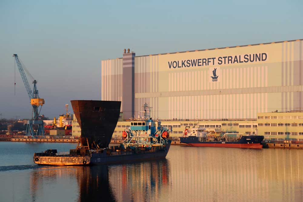 Transportschiff „Aura“ mit dem Vorschiff der „Walther Herwig“ vor der Montagehalle 290 in Stralsund; hinten rechts der Tanker „Annika“