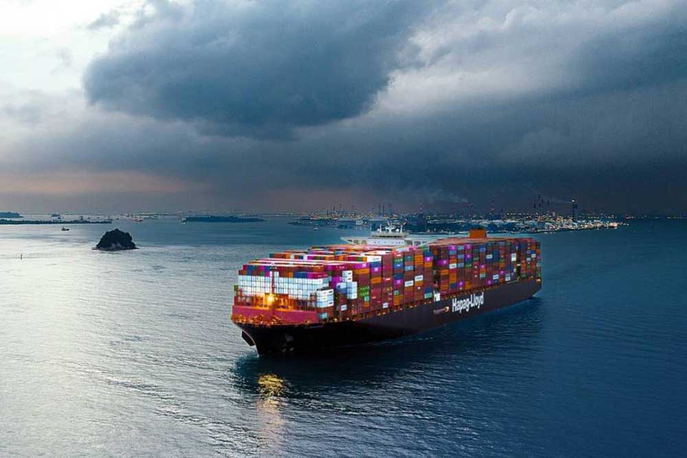 Containerschiff vor einem Hafen, im Hintergrund ein Gewitter