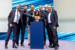 Sieben Menschen vor einem Podium, die zusammen auf einen Knopf drücken