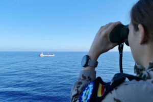 Ein Person beobachtet ein Frachtschiff auf dem Mittelmeer